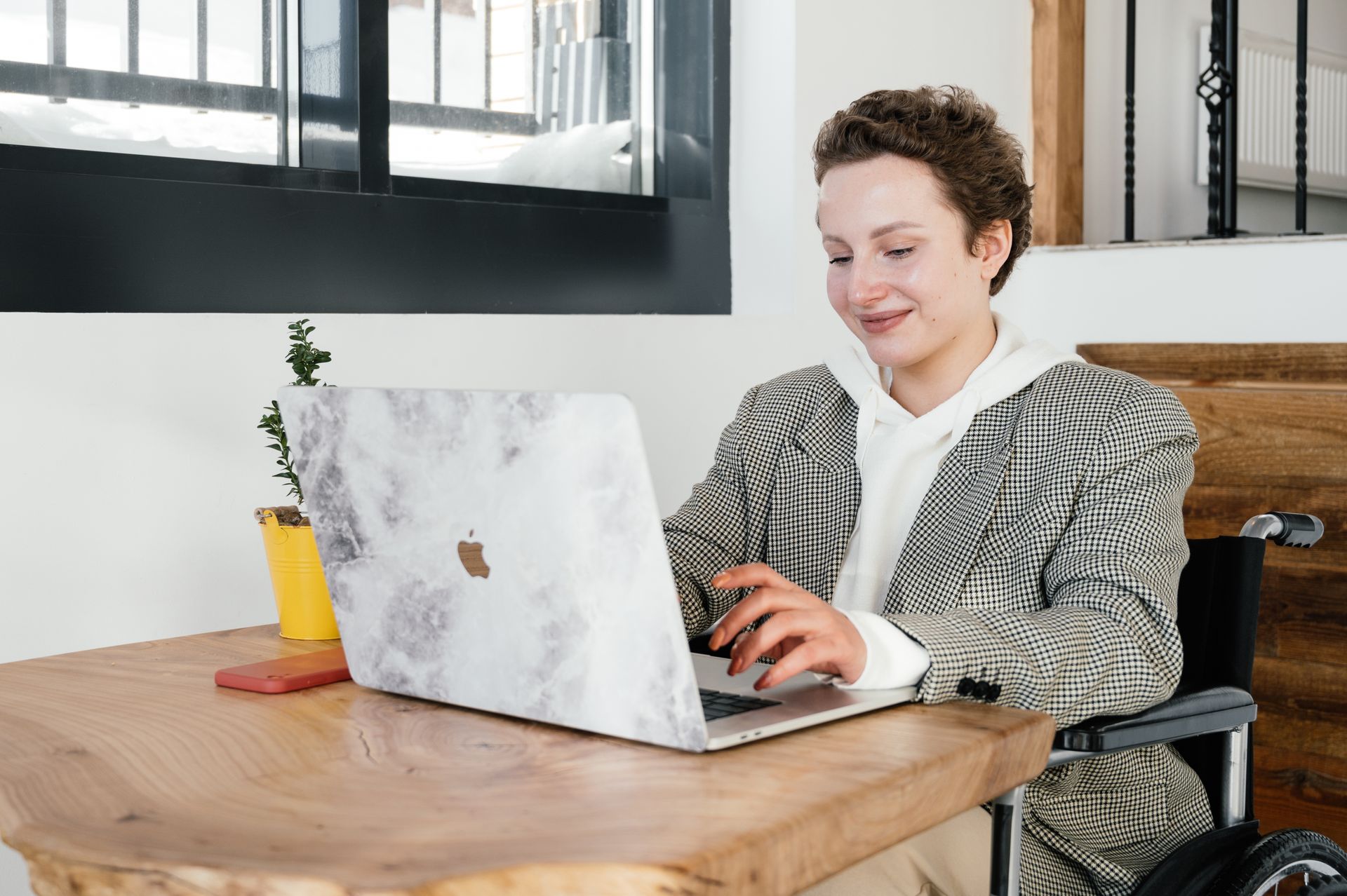 Woman in wheelchair typing on laptop at a café, embodying modern remote work and independence.