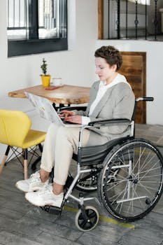 A young woman in a wheelchair working on a laptop in a modern cafe setting.