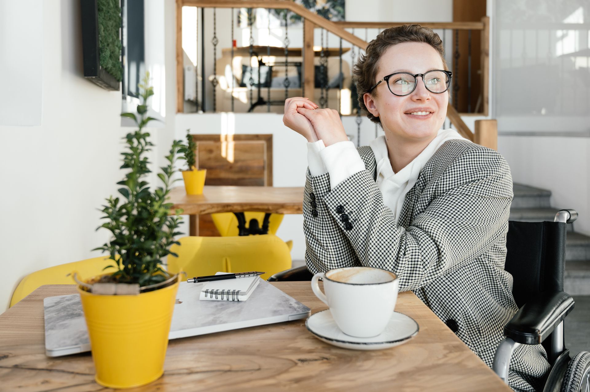 A woman in a wheelchair enjoys a coffee break at a bright and welcoming café.
