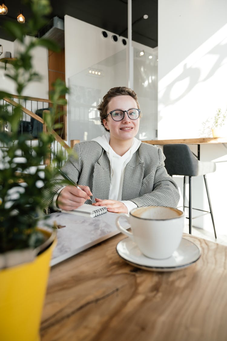 Smiling Woman Writing In Notebook In Cafe