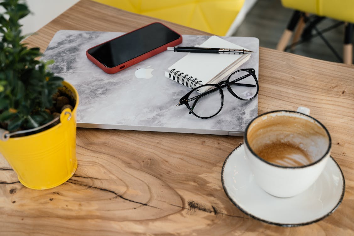 Free High angle contemporary laptop and smartphone placed on table near cup of half finished cappuccino and copybook in cafeteria Stock Photo