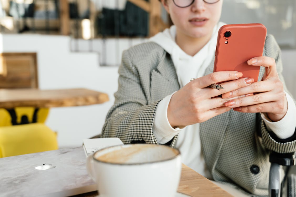 Free Crop focused female in formal wear and eyeglasses browsing mobile phone while having coffee in cafeteria Stock Photo