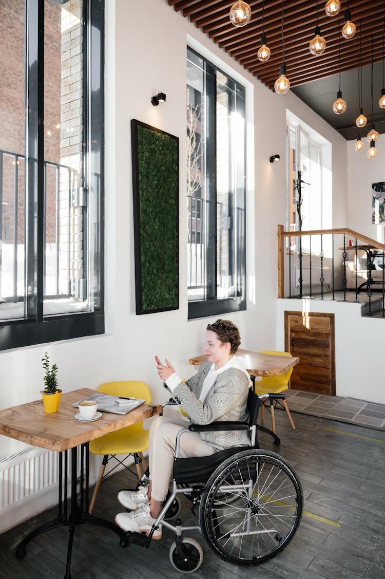 Calm Woman In Wheelchair Using Smartphone In Cafeteria