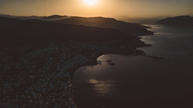 A breathtaking aerial view of a coastal city silhouetted by the setting sun over the horizon.