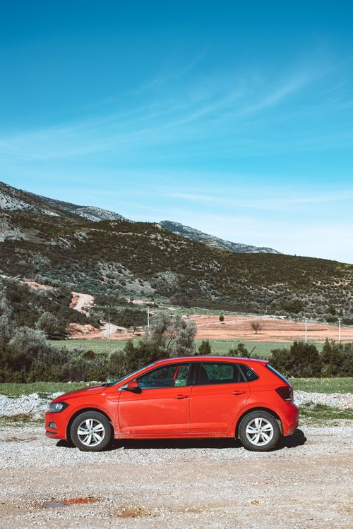 Free Vibrant red car parked against a beautiful countryside backdrop with clear blue sky. Stock Photo