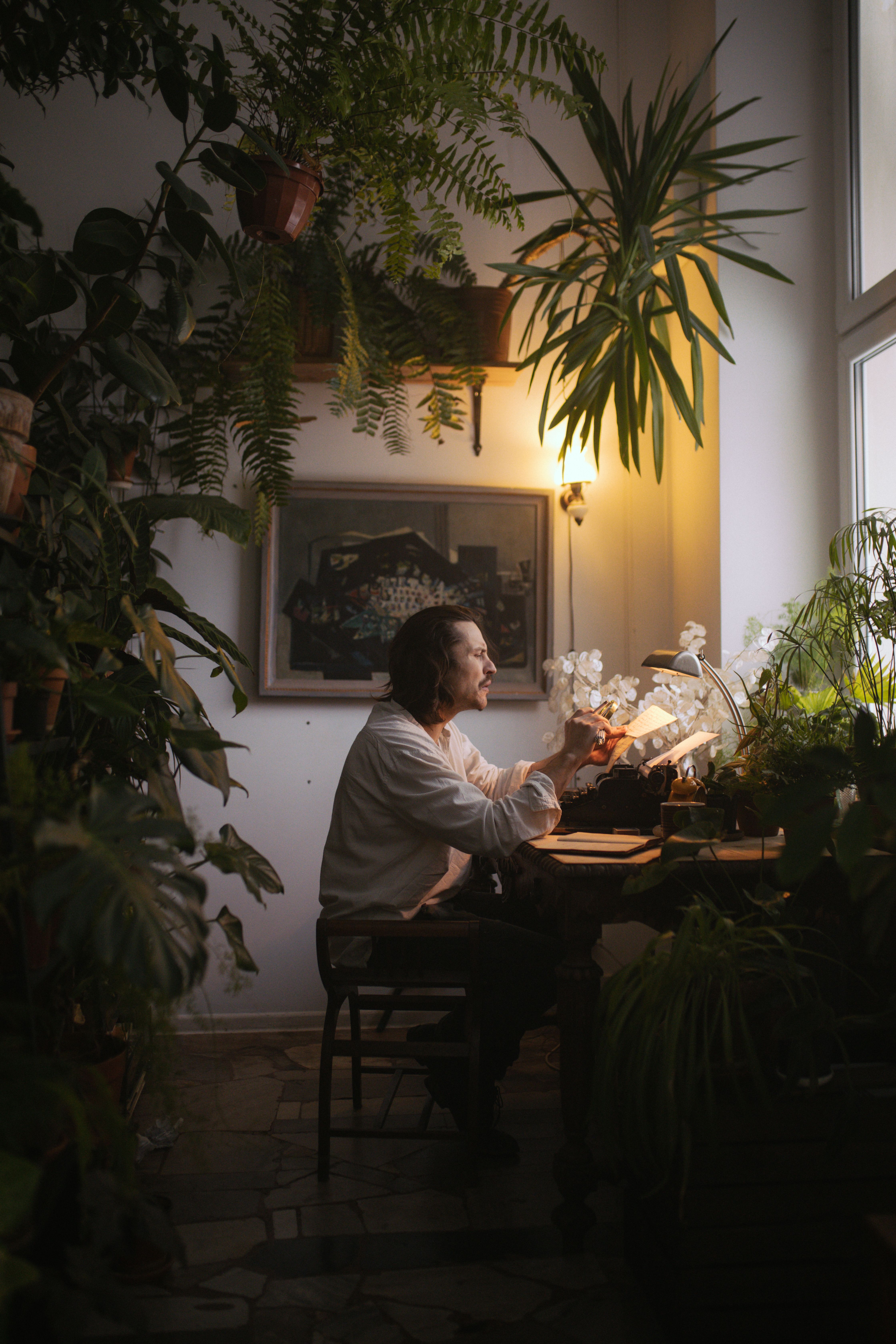 A man sits at a desk surrounded by lush indoor plants, creating a tranquil workspace.