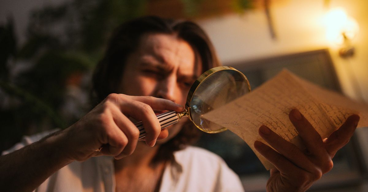 A teenager looking at a laptop with a skeptical expression, holding a magnifying glass