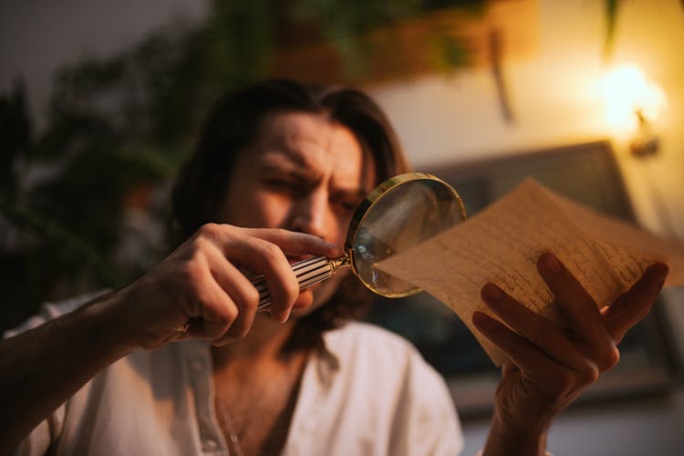 A Man Looking At A Paper Through A Magnifying Glass