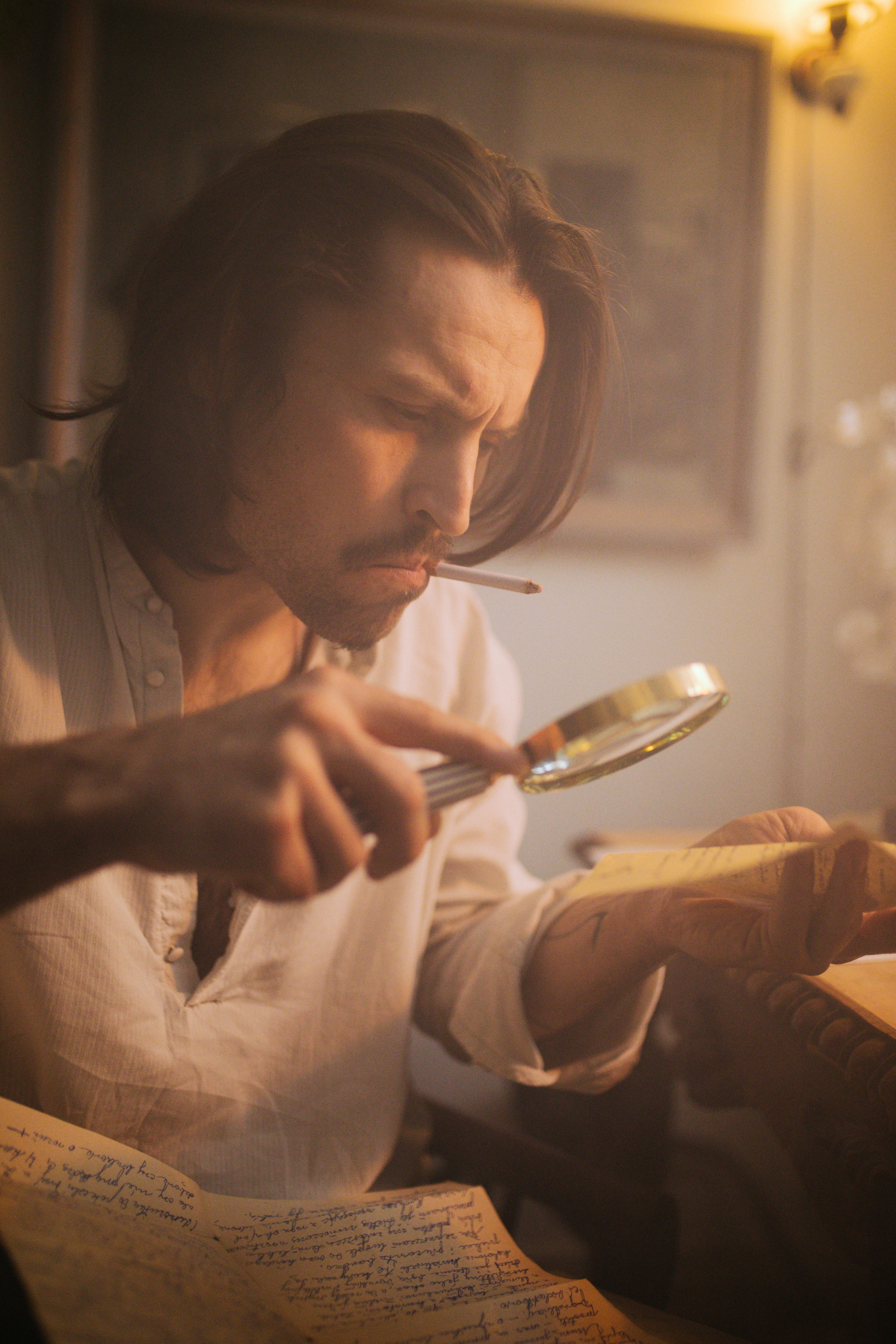 Vintage style image of a man indoors examining letters with a magnifying glass and smoking.