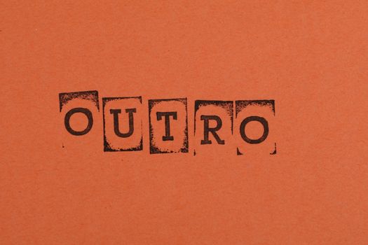 Close-up of the word OUTRO stamped on orange paper, highlighting typography and design.
