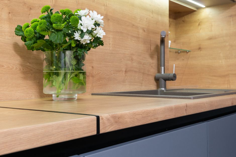 Blossoming chrysanths in vase with water on wooden table against sink with tap in contemporary kitchen at home