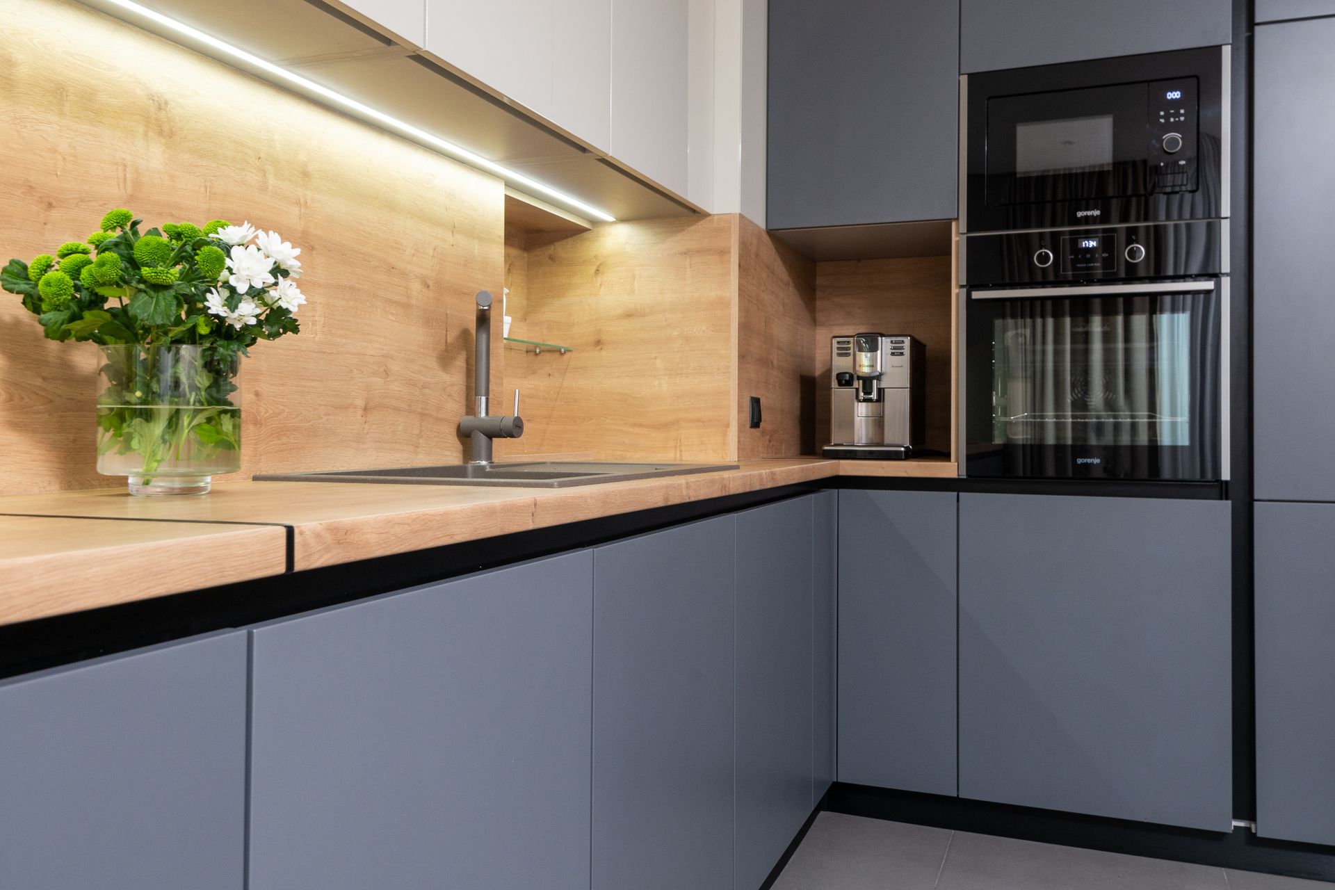 Cabinets with coffeemaker against oven and table with blooming flowers in vase in modern kitchen