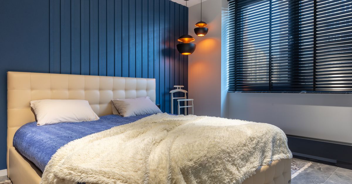A bed made up with a soft cream fleece blanket over a blue comforter in a calm bedroom