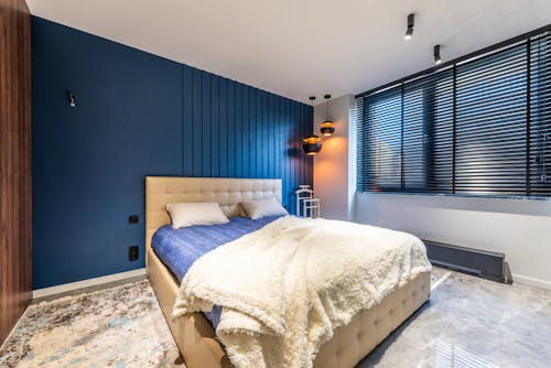 Plaid with pillows on bed against lamps and window blinds above tiled floor in contemporary bedroom