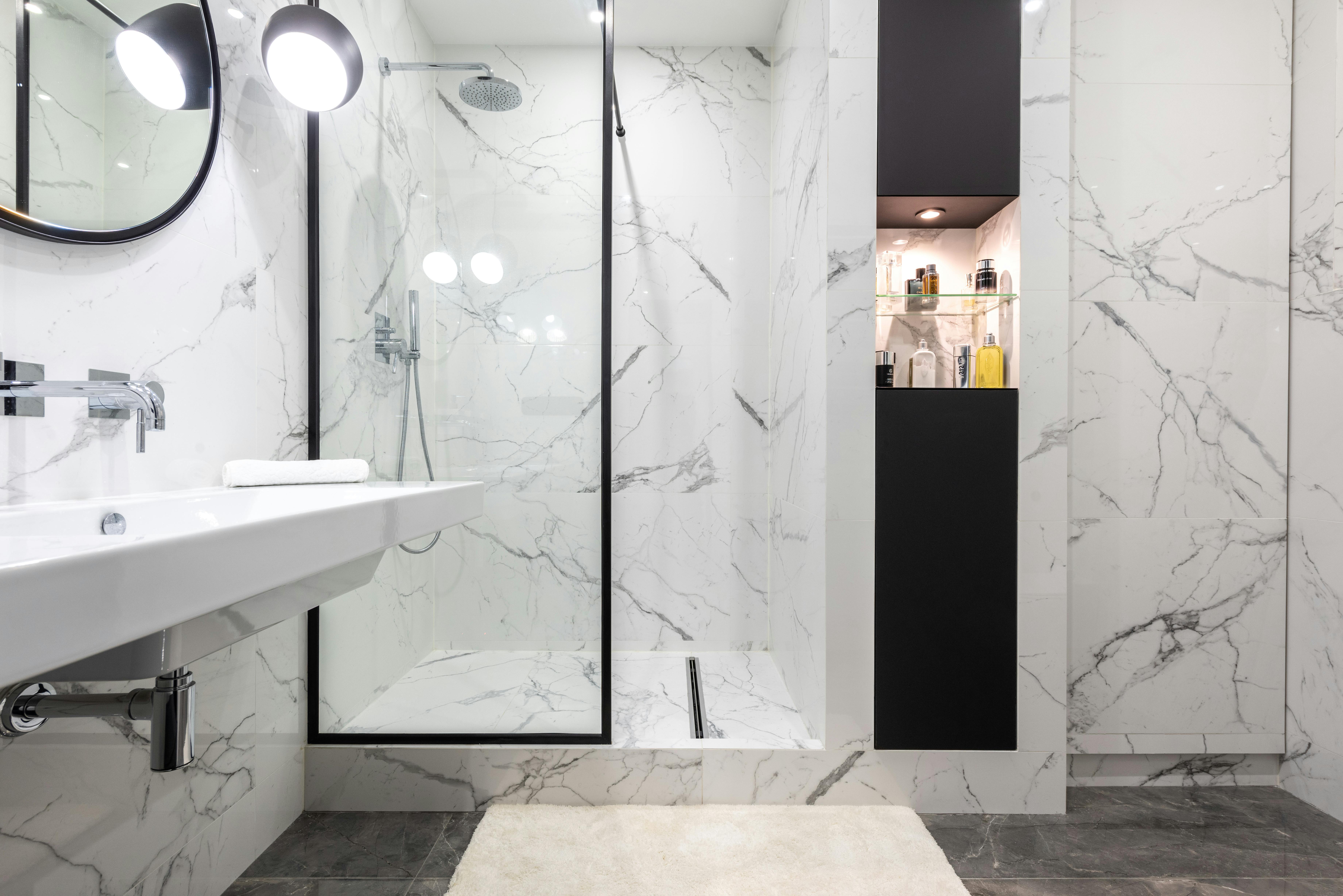 Modern bathroom interior with shower room against bottles of perfumes and washbasin under mirror reflecting shiny lamp in house