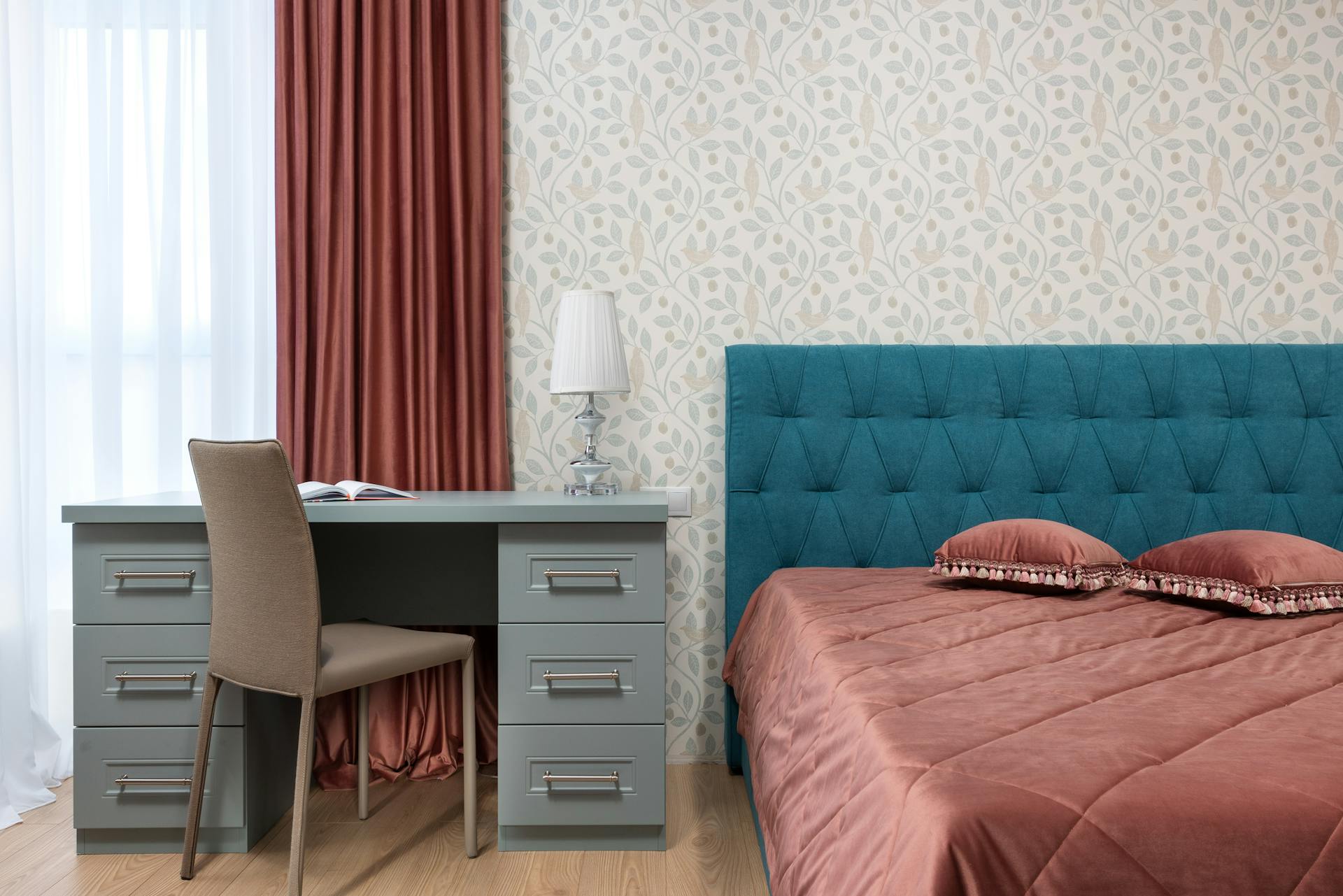 Bed with cover and cushions against lamp on table and leaf ornament on wall in light house
