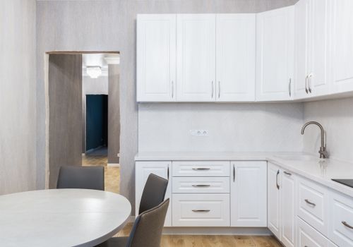 Free Contemporary kitchen interior with white cupboards and tap against table with chairs on parquet in light house Stock Photo