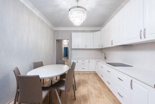 Free White cabinets and built in stove against oval shaped table with chairs illuminated by chandelier at home Stock Photo