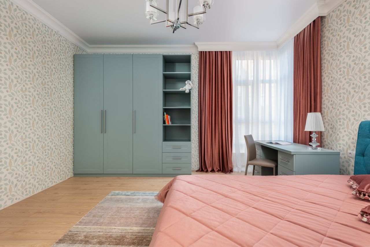 Sage-green bedroom wardrobe with open display shelves, a desk, and coral bedding
