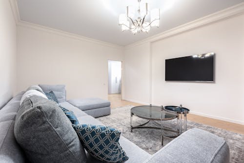 Contemporary room interior with couch and TV with black screen against tables under shiny chandelier in house