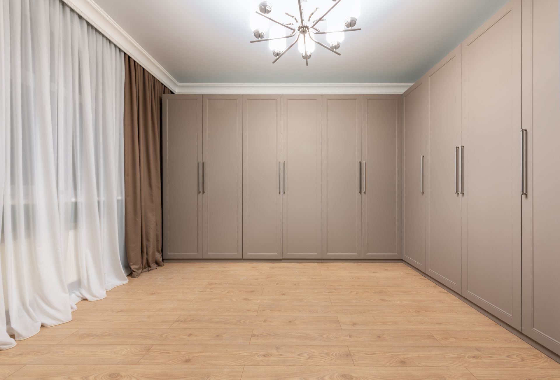 Contemporary minimalist closet interior with beige cabinets and wooden flooring.