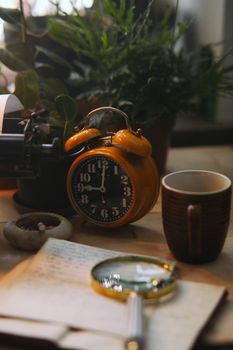 Cozy vintage desk scene with a yellow twin bell alarm clock, mug, and plants.