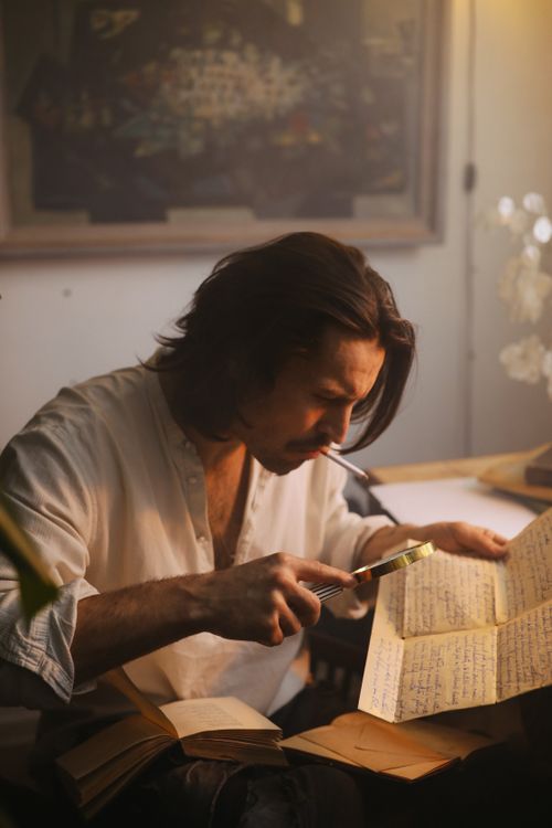Free Caucasian man using magnifying glass to read paper in cozy indoor setting. Stock Photo