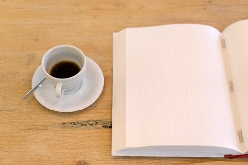 White Ceramic Coffee Cup and Saucer Near a Journal Book