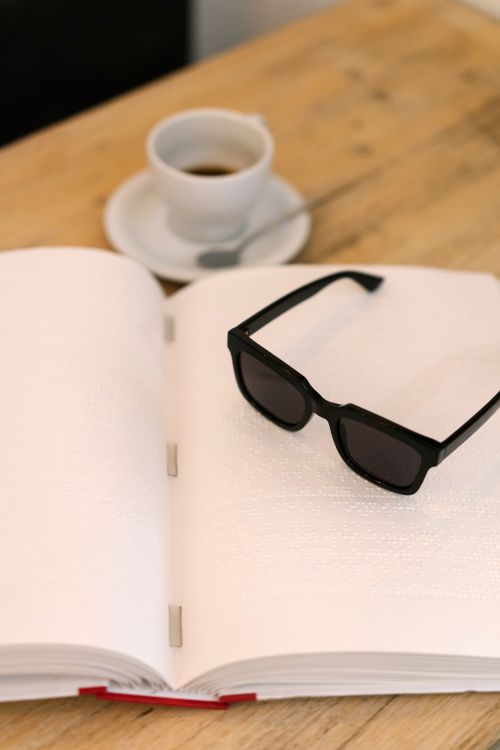 Free An open Braille book with sunglasses and coffee cup on a wooden table, offering a tactile reading experience. Stock Photo