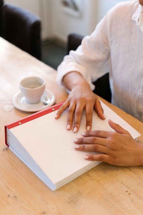 Free Close-up of a person reading a Braille book with a coffee on the table. Stock Photo