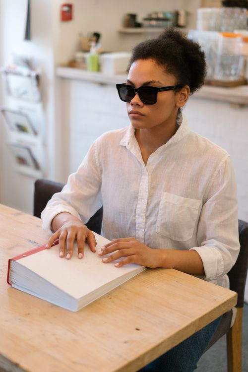 Free An African American woman reading a braille book indoors, focusing on her tactile interaction. Stock Photo