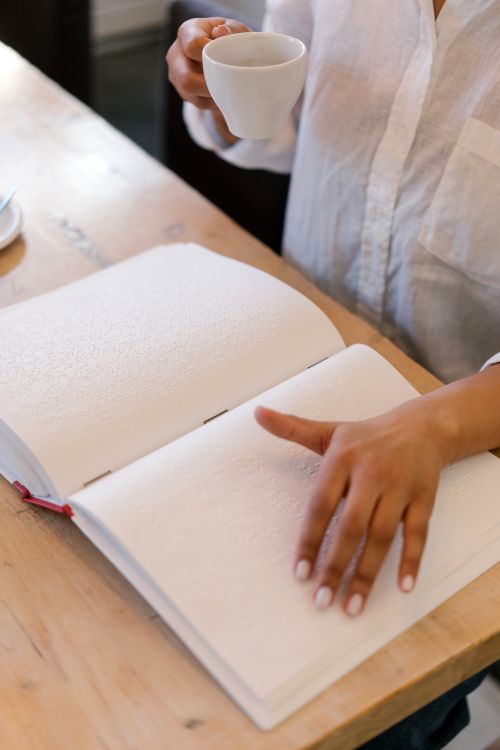 Free Close-up of a person reading a Braille book while holding a cup of coffee, highlighting touch. Stock Photo