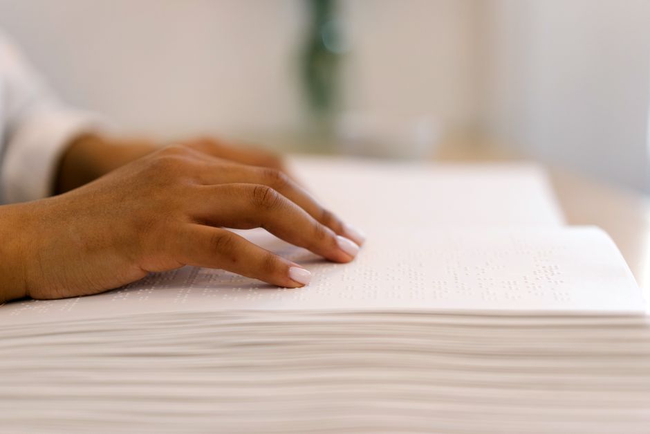 Close-up of a person's hand reading a Braille book, highlighting accessibility and tactile reading.