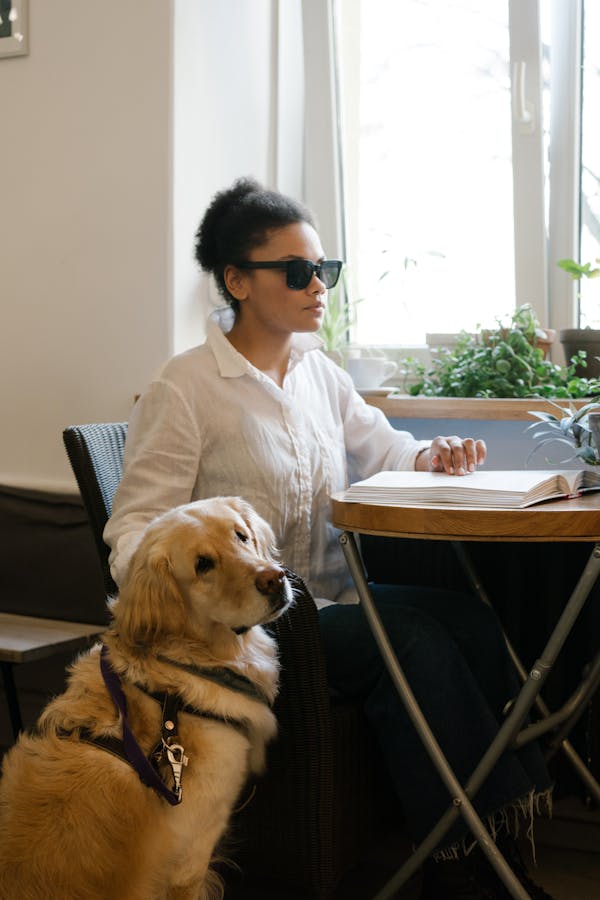 female reading braille book with service dog at her side