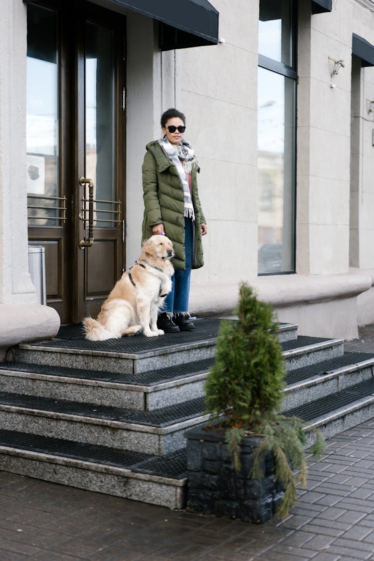 A Woman Standing Beside Her Guide Dog Outside A Building