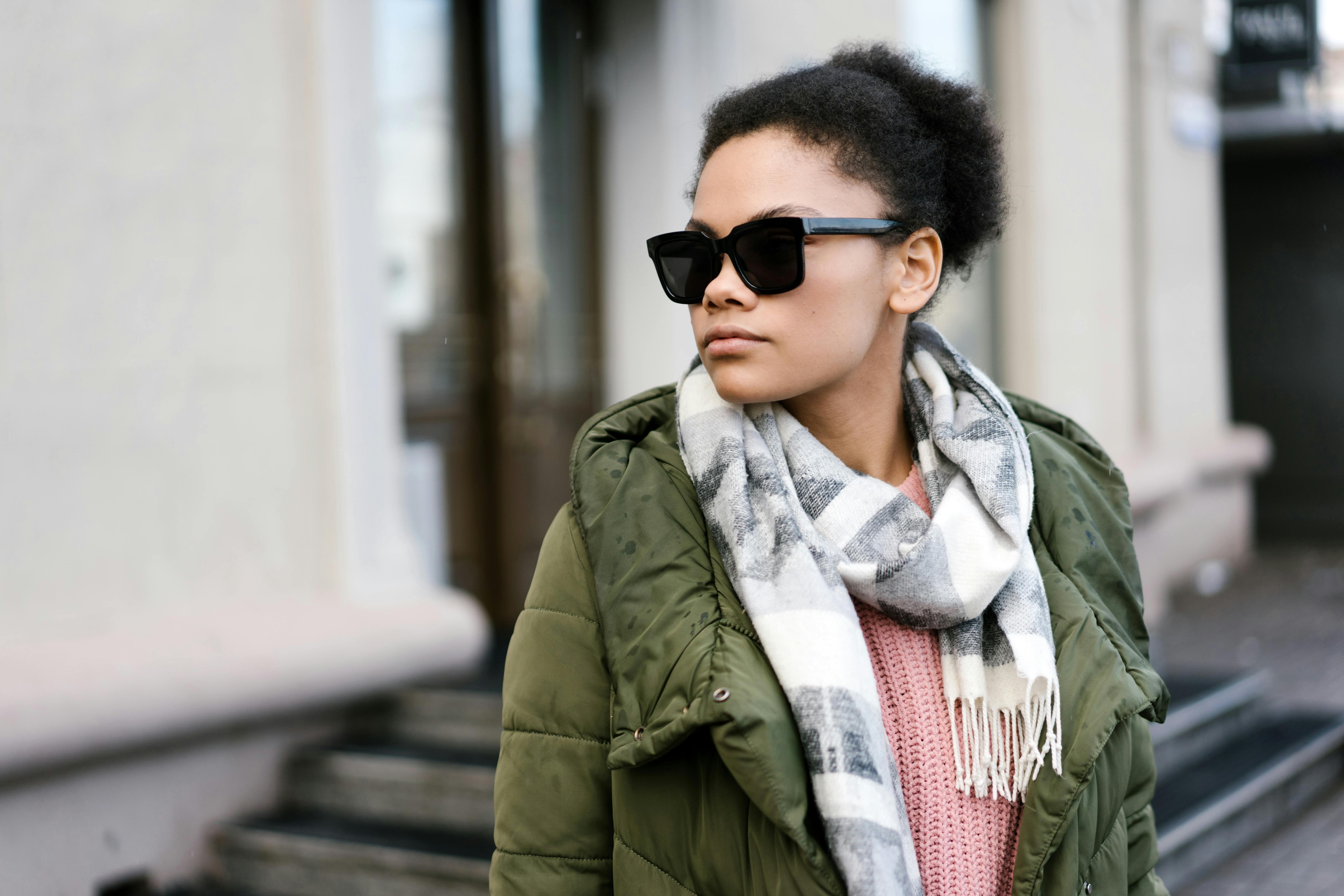 Young woman in winter clothing with sunglasses standing outside a building.