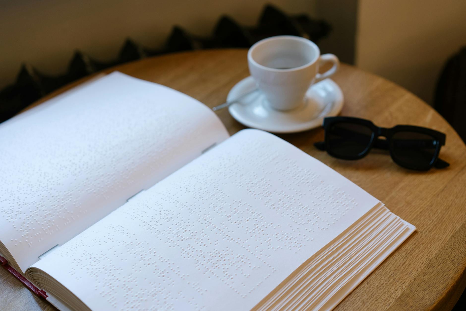 Open braille book with coffee cup and sunglasses on a table symbolizing accessibility.