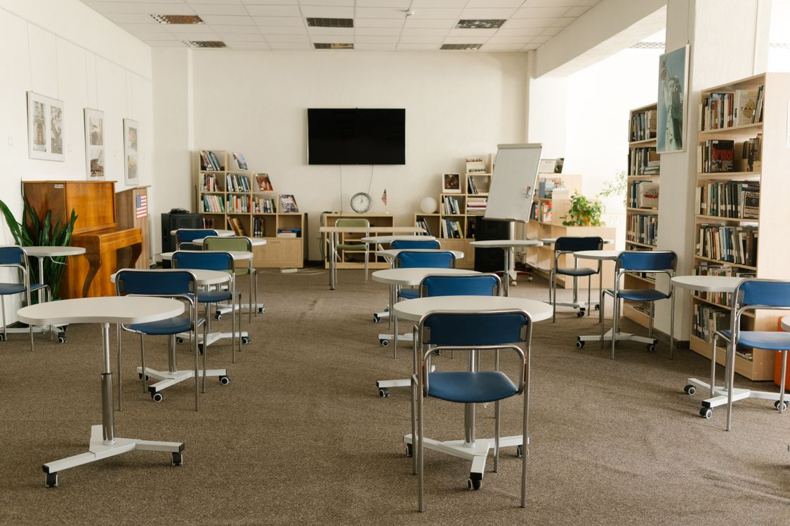 Tables and chairs arranged inside a carpeted classroom.