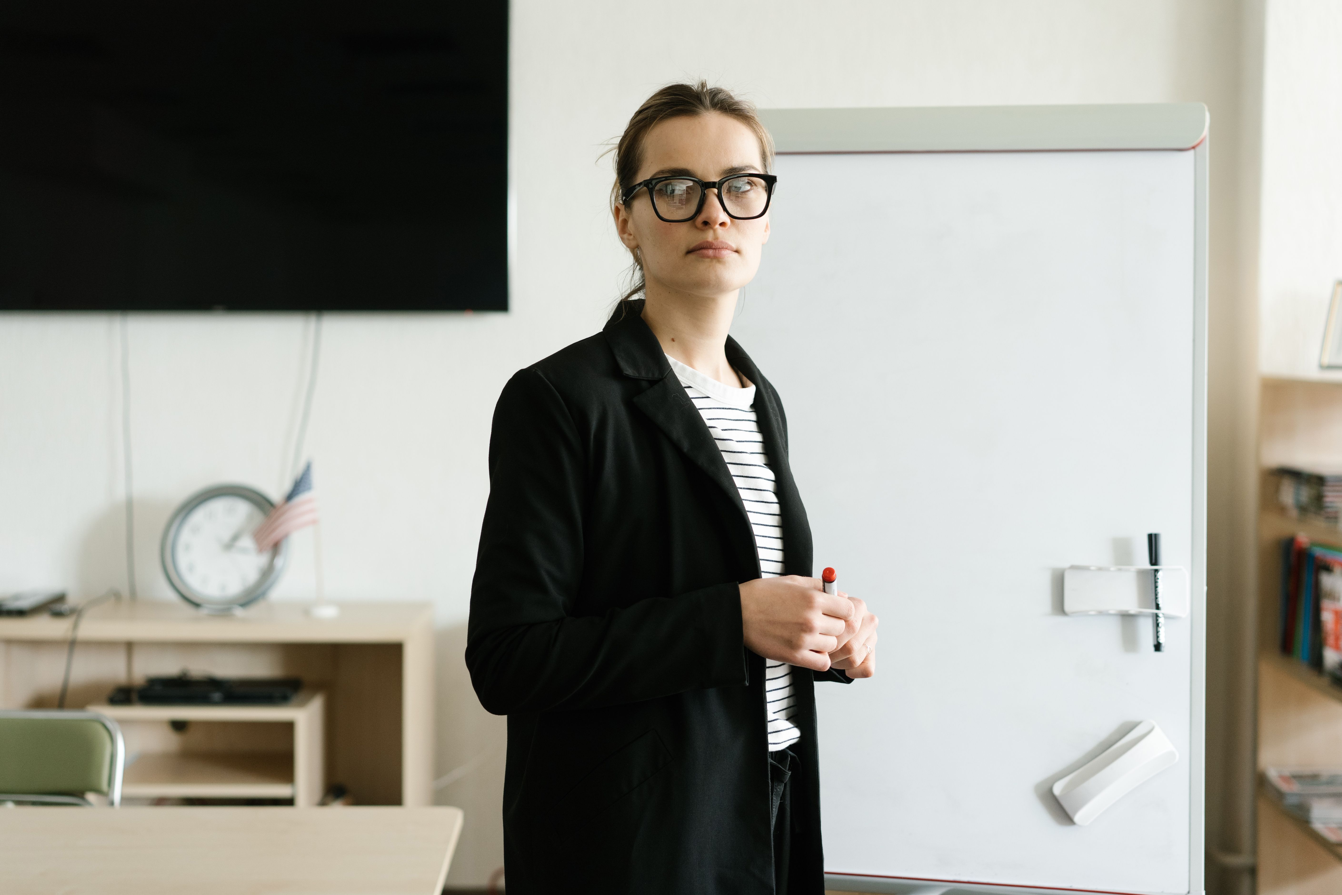 Businesswoman in formal attire standing by a whiteboard in an office setting, ready for a presentation.