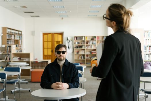 Blind student engaged in classroom discussion with teacher. Inclusive education setting.