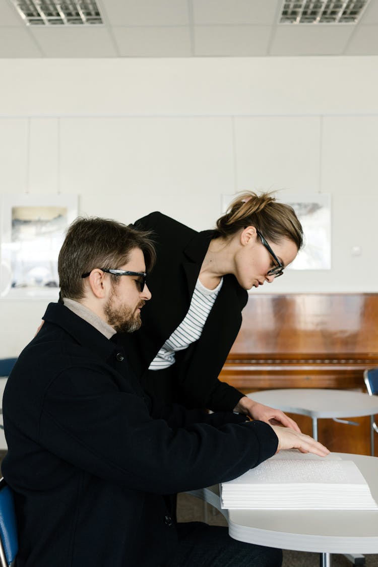 A Woman Helping A Man In Black Suit Touching A Braille