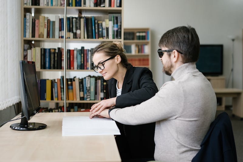Caregiver helping a visually impaired person read Braille in a library