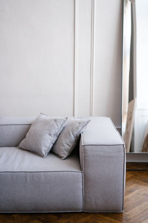 Free A chic gray sofa in a stylish, minimalist living room with a large mirror and elegant decor. Stock Photo