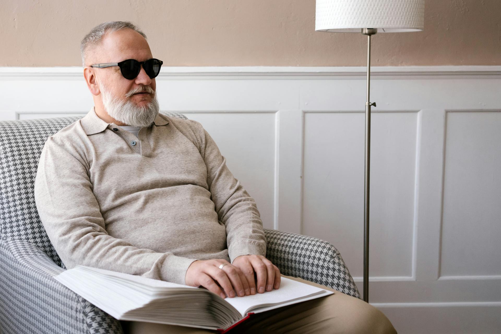 Elderly man reading a Braille book, representing accessibility and vision impairment awareness.