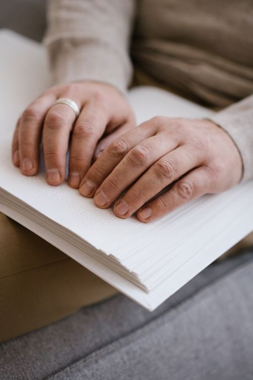 Free Close-up image of hands using Braille to read a book, symbolizing accessibility and disability support. Stock Photo