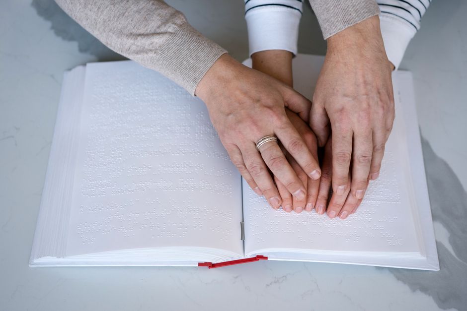 点字本を読む手のクローズアップで、触覚学習と視覚障害サポートを強調しています。