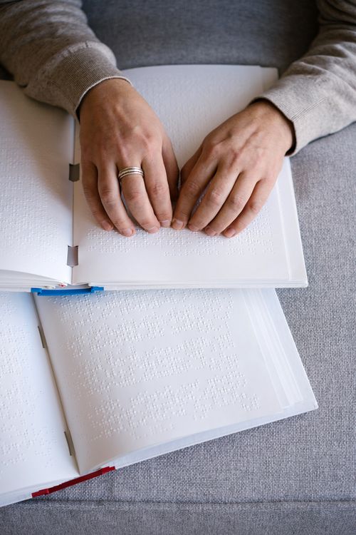 Free Hands reading Braille text on an open book, representing tactile reading and accessibility. Stock Photo