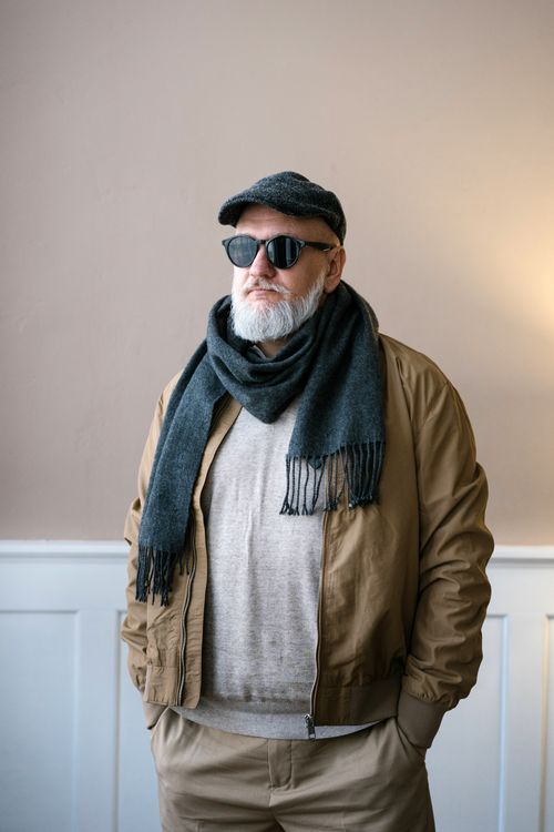 Free Cool senior man with a beard and sunglasses, dressed in casual attire with a scarf, exuding confidence indoors. Stock Photo