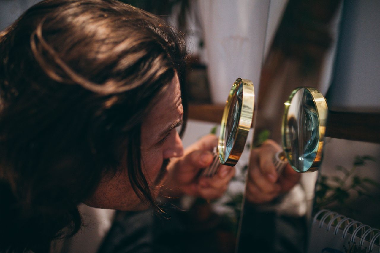 close up shot of a man with long hair using a magnifying glass to insp