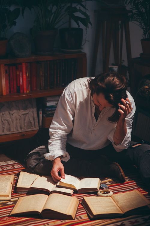 Free Man reading books in a cozy indoor setting with plants and shelves. Stock Photo